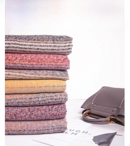 Detail shot of soft multi-color striped knitted scarves with fringe stacked on a white surface