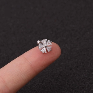 Macro detail of a silver flower ear stud with zircon stones held on a fingertip