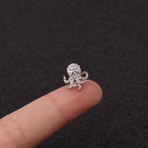 Macro shot of silver octopus stud earring with clear zircon crystals on fingertip