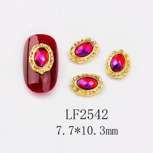 Macro detail of red oval nail art gem with vintage gold relief frame on white background