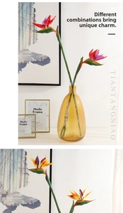 Detail of red and orange bird of paradise silk flowers in an amber glass vase
