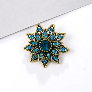 Elegant gold flower brooch with blue crystal rhinestones on a white background