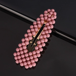 Close-up of pink matte pearl snap hair clip with golden metal base on dark reflective surface