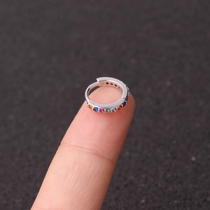 Miniature silver huggie earring with multicolor zircon crystals shown on fingertip