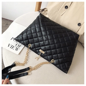 Detail of black quilted tote bag with golden chain strap and a small elk pendant charm
