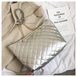 Close-up of silver quilted tote bag featuring a golden deer charm and chain strap