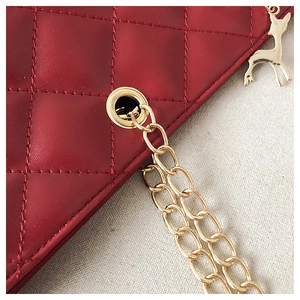 Close-up of red quilted leather bag with gold chain and deer-shaped pendant charm