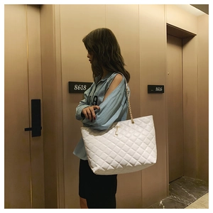 Detail of white quilted tote bag featuring golden chain strap and small deer metal charm