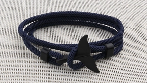 Detailed view of a dark blue braided cord bracelet featuring a black whale tail clasp