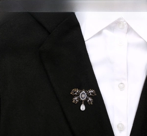 Detail view of a vintage bow brooch with pearl pendant on a black blazer lapel