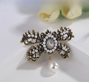 Macro shot of retro gold bow brooch featuring white pearls and a grey gemstone center
