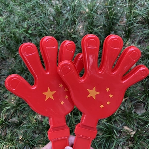 Détail de main applaudissante en plastique rouge avec étoiles sur herbe verte