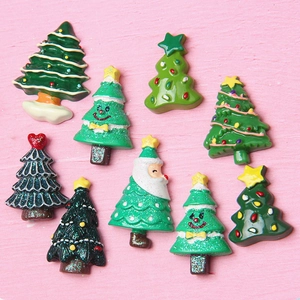 Assorted green Christmas tree resin charms with flatback design on pink wood surface