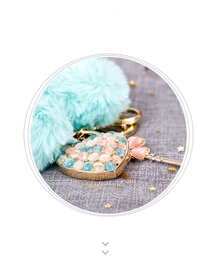 Detail of heart pendant with pink stones, blue fur ball, and gold key on a keychain