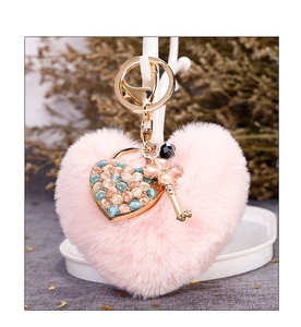 Detail of pink heart pompom keychain with golden clover key and colorful gemstone charms