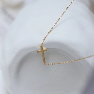 Dettaglio della collana con croce d'oro minimalista su piatto di ceramica bianca
