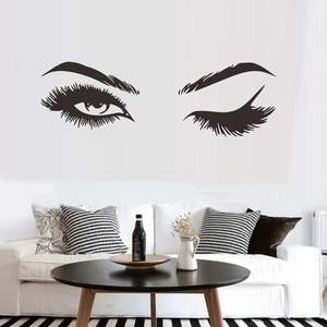 Zwarte vinyl muursticker met ogen en wenkbrauwen boven een moderne witte bank in een woonkamer