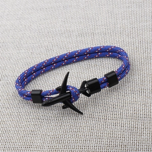 Detail of blue paracord bracelet with a black airplane charm on beige textured fabric