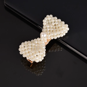 Detailed view of pearl woven bow hair clip with gold metal clasp on reflective surface