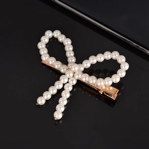 Detailed shot of a pearl bow hairpin with white imitation pearls on a gold metal base