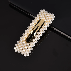 Detail view of a golden rectangular hair clip with white pearls on a black surface