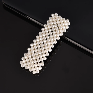 Detail view of woven pearl hair clip with white artificial pearls on a black background