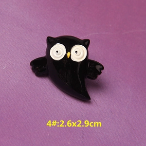 Macro detail of black resin owl brooch pin for DIY accessories on purple fabric background