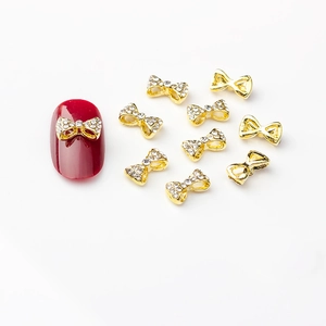 Nœuds dorés pour nail art avec strass scintillants sur un fond blanc épuré