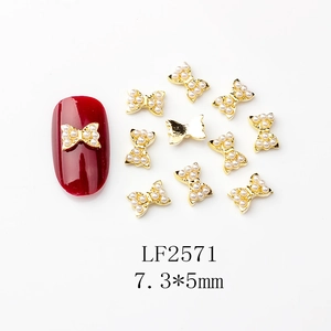 Vue macro de bijoux d'ongles nœuds dorés avec perles sur ongle rouge foncé, 7,3*5mm