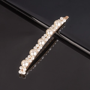 Close-up of elegant pearl hair clip with gold metal base on a reflective black surface