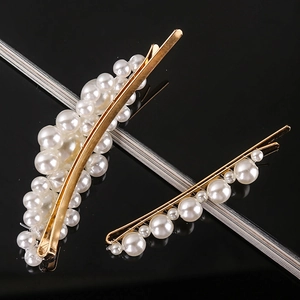 Detailed view of two gold-finish hair clips with elegant clustered white pearls on black background