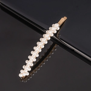 Detailed macro view of white faux pearls inlaid on a gold alloy hair clip on black surface