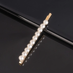 Close-up of gold metal hair clip featuring evenly arranged white pearls on a black surface