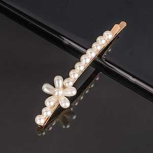 Macro shot of gold-plated hair clip featuring pearl flower design on a black reflective surface