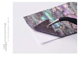 Macro shot of 3D iridescent shell nail sticker being peeled with tweezers