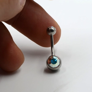 Macro shot of G23 titanium navel piercing with multi-color faceted crystal and curved barbell