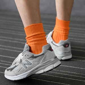 Vibrant orange cotton crew socks worn with classic grey suede sneakers for street style