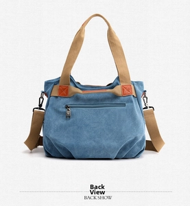 Detail of blue canvas shoulder bag back view showing metal zipper pocket and webbed straps