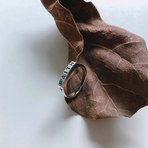 Macro shot of silver Faith cross open ring resting on a textured autumn leaf detail