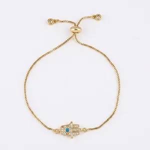 Detailed close-up of gold Hamsa hand bracelet with white pavé stones and blue evil eye charm