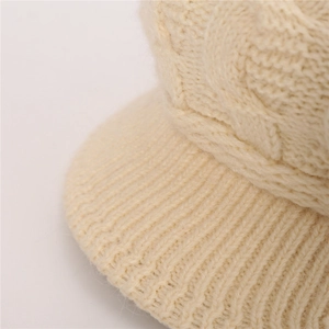 Detalle de punto de ochos crema y visera en un gorro de invierno grueso para mujer