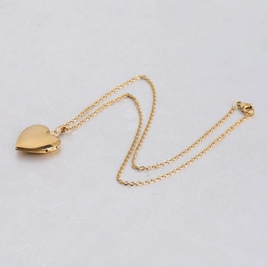 Polished gold heart locket necklace with delicate chain on a textured grey background