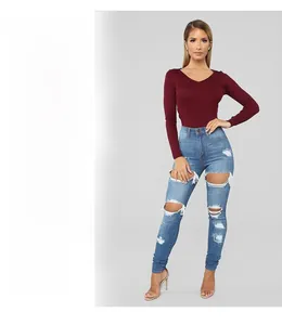 Detail of ripped skinny blue jeans paired with a ribbed V-neck long sleeve burgundy top
