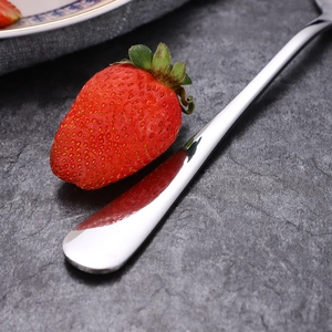 Polished stainless steel spoon reflecting a fresh strawberry on a dark stone background
