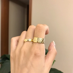Close-up of gold layered rings with openwork flower and quilted pattern on hand