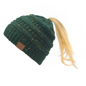 Dettaglio cappello in maglia verde scuro con foro per coda di cavallo e toppa in cuoio