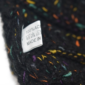 Dettaglio del berretto in maglia nera con puntini colorati ed etichetta di lavaggio
