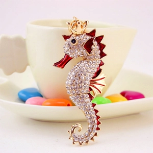 Sparkling seahorse keychain with gold crown and red enamel accents on a sweet background