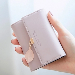 Detailed view of pale pink mini wallet with decorative gold ring and leaf charm
