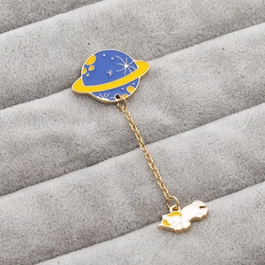 Detail of blue and yellow planet enamel pin with a hanging white space cat pendant